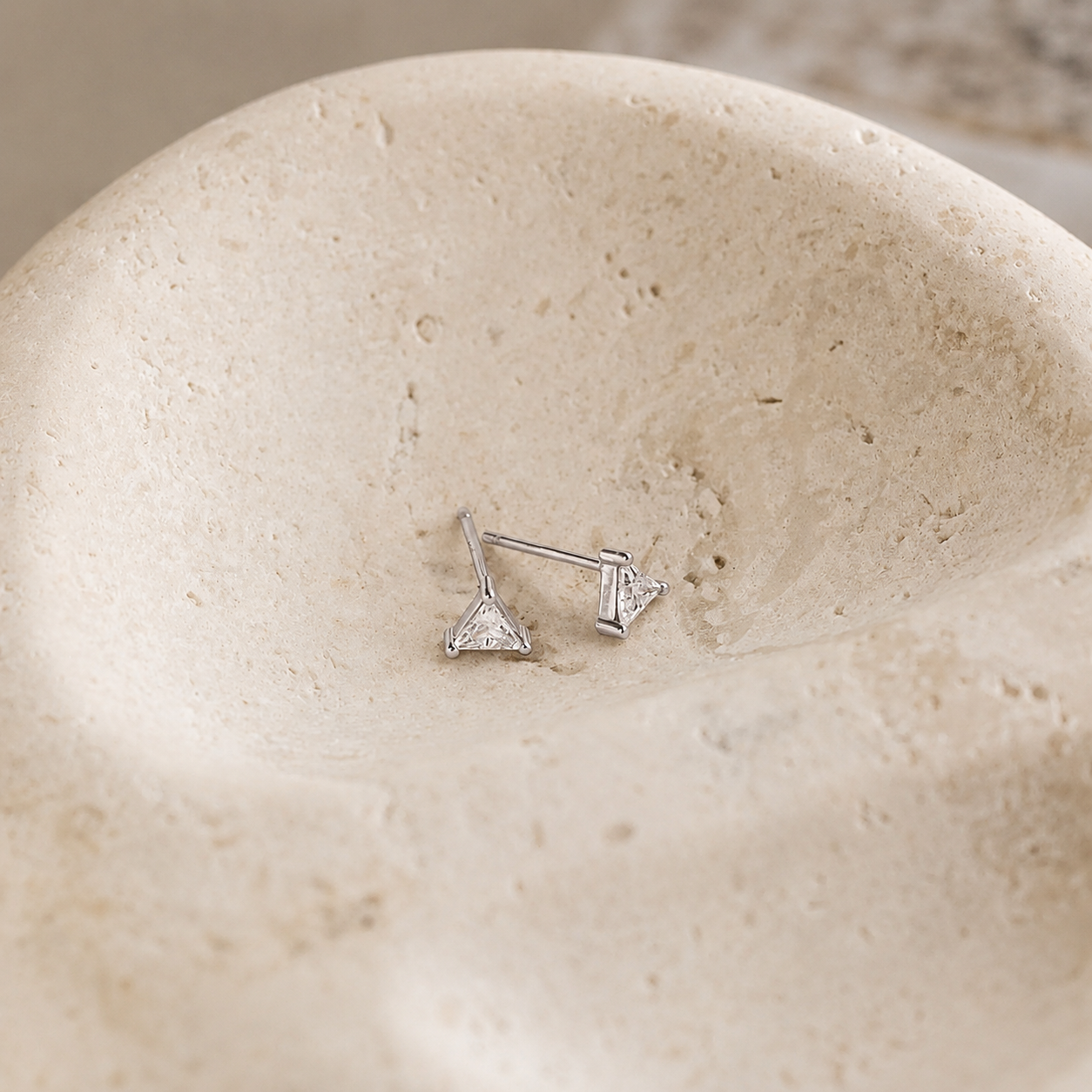 Pair of silver arrow-shaped earrings on a beige stone surface