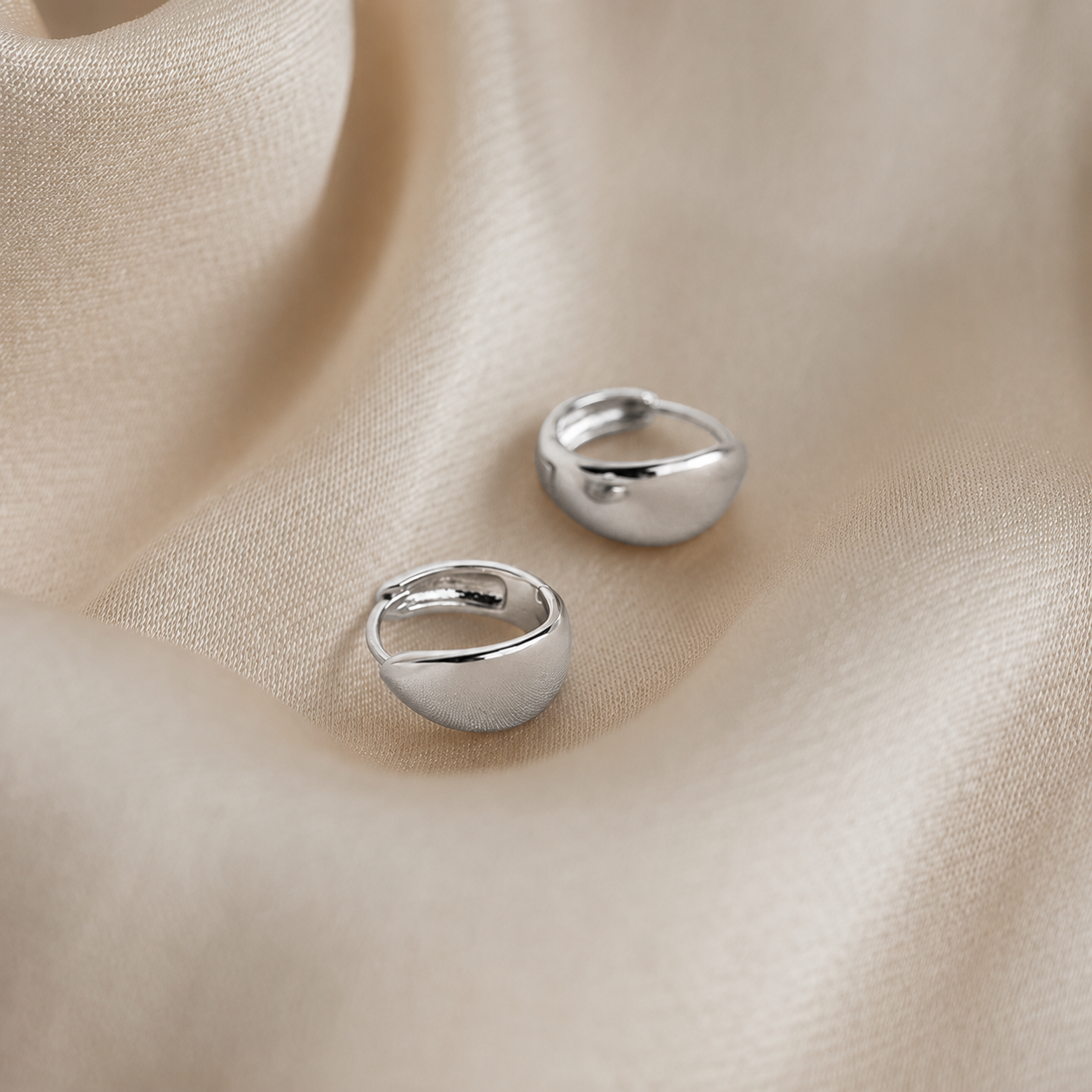 Two silver rings on a beige fabric background