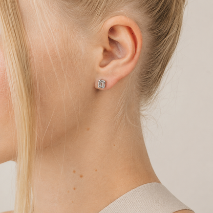 Close-up of a person wearing a silver stud earring on a neutral background