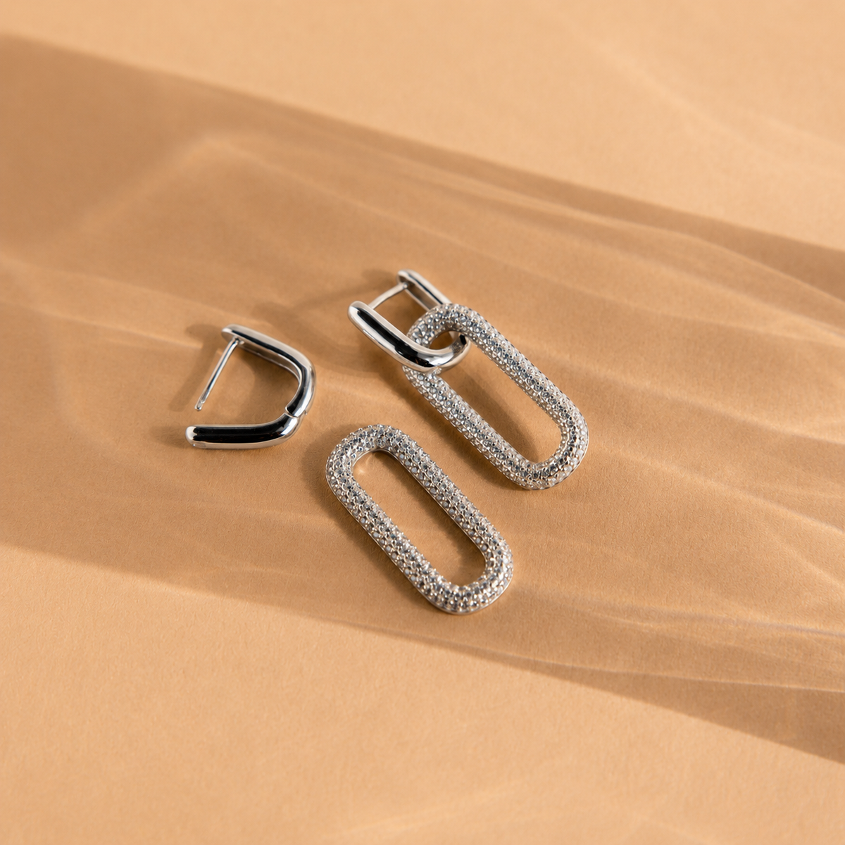 Silver hoop earrings on a beige sand-like background