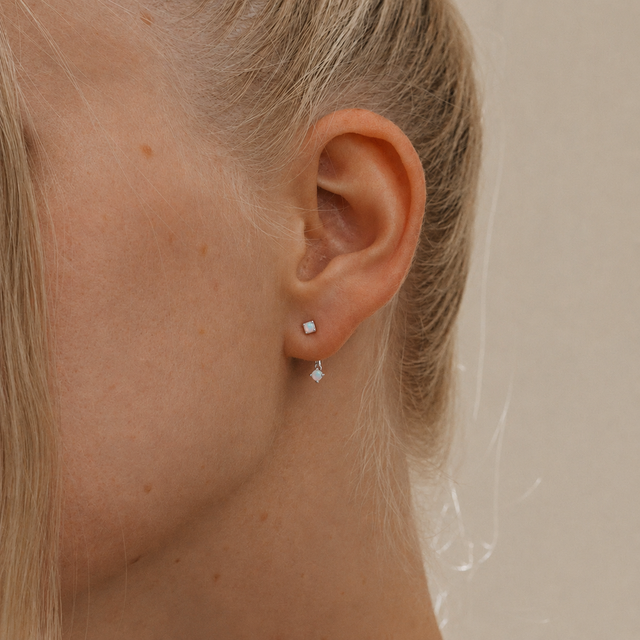 Close-up of an ear wearing diamond stud earrings with a neutral background