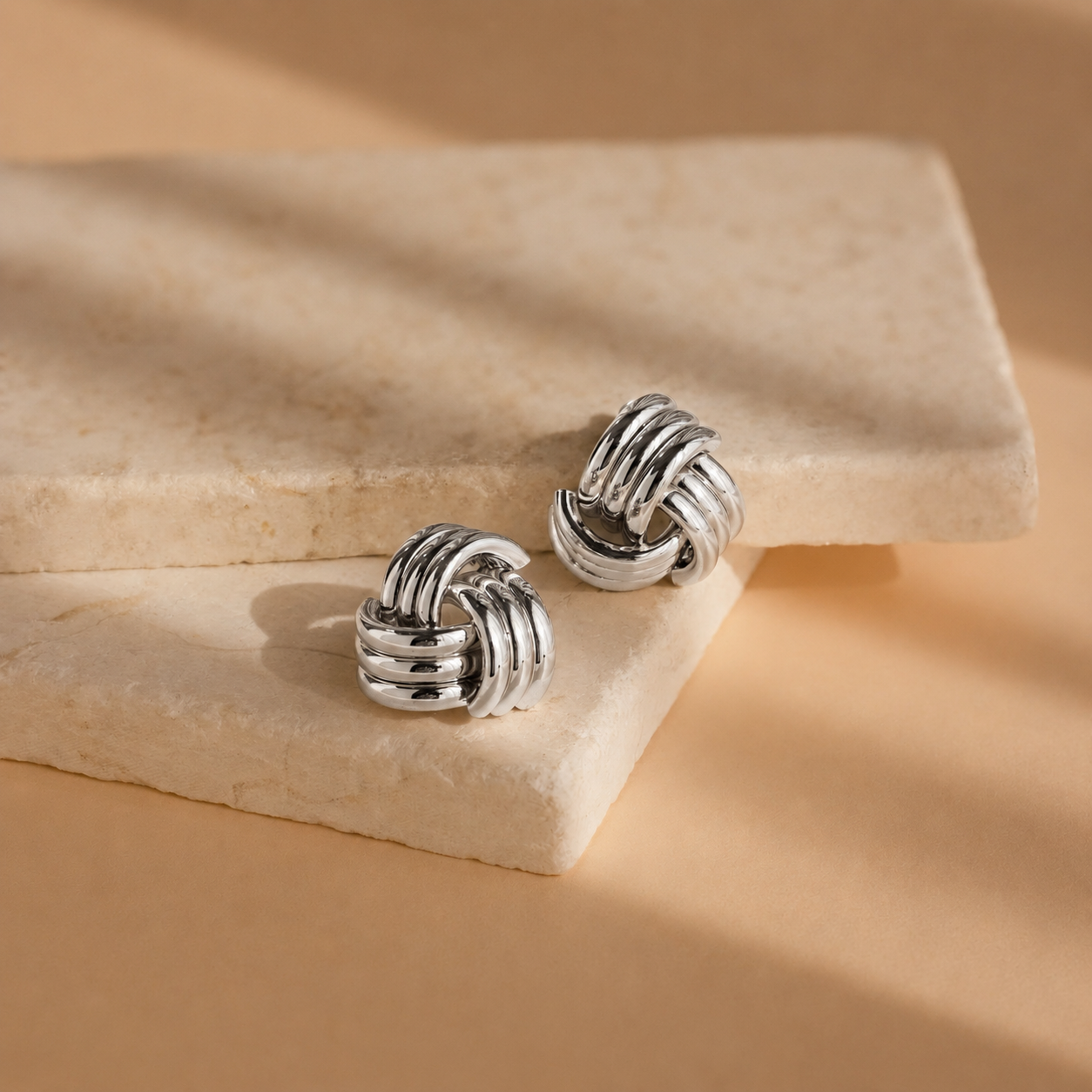 Pair of silver knot earrings on a beige stone surface