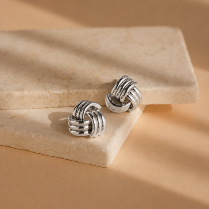 Pair of silver knot earrings on a beige stone surface