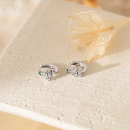 Silver earrings with green gemstones on a textured beige surface