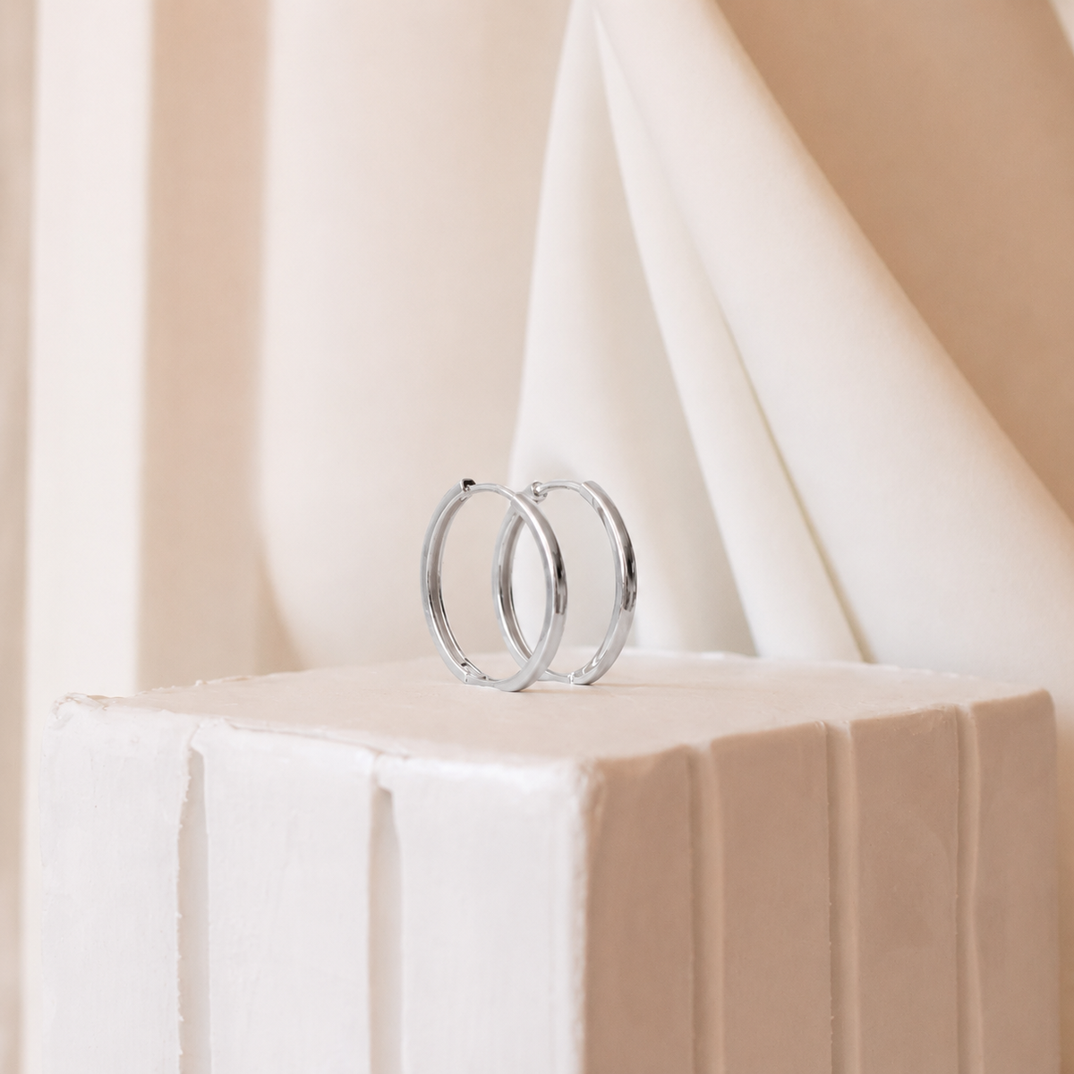 Silver hoop earrings on a white and beige geometric surface