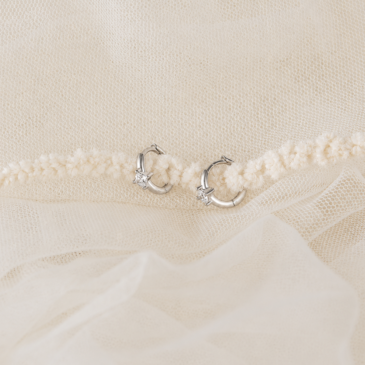Silver hoop earrings on a textured beige fabric background