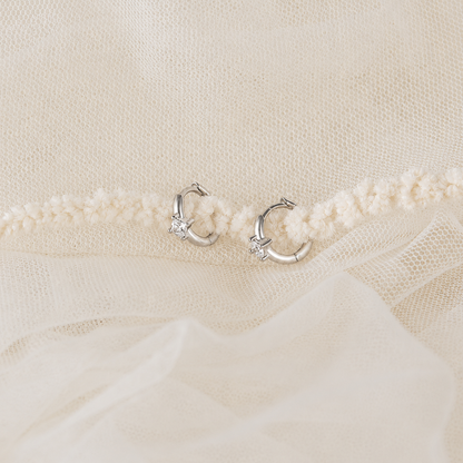 Silver hoop earrings on a textured beige fabric background