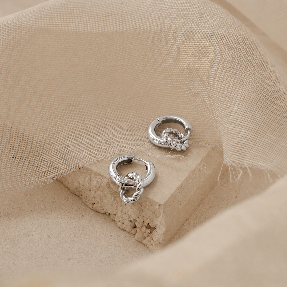 Pair of silver hoop earrings on a beige fabric background