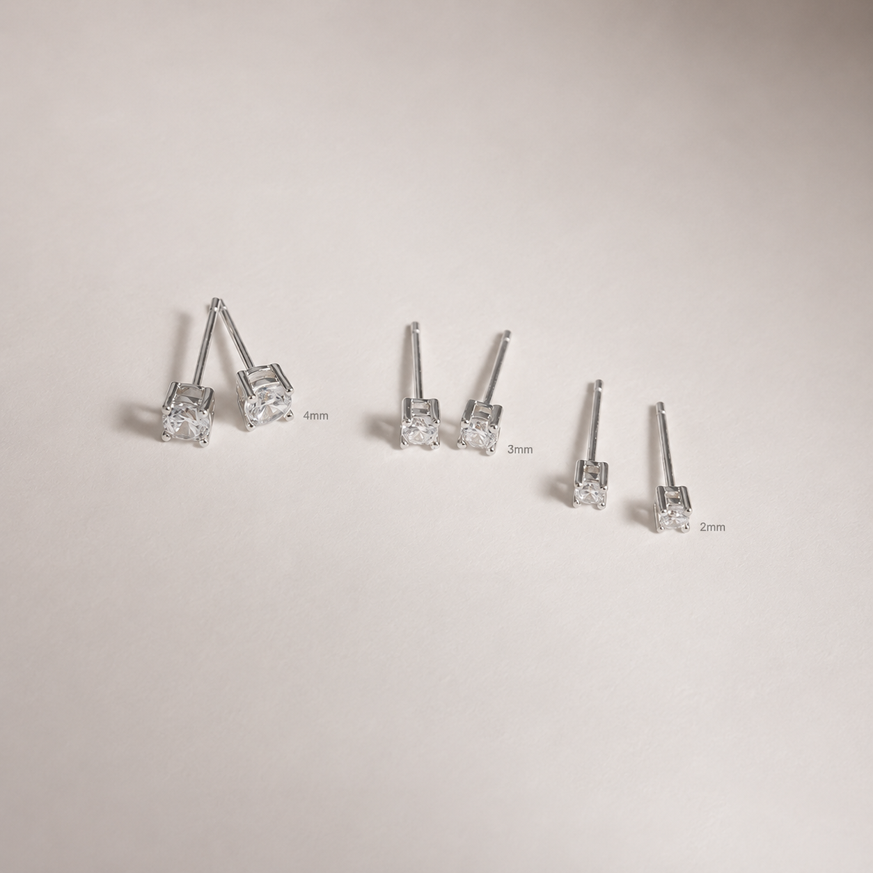 Set of diamond stud earrings with size labels on a light gray background