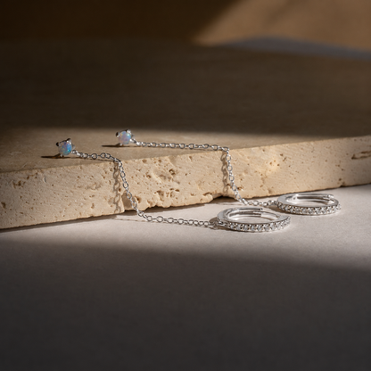 Silver jewelry set including earrings and a necklace on a textured surface.