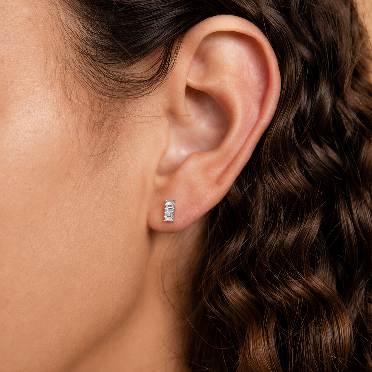 Close-up of an ear wearing a diamond earring with hair partially covering the side.