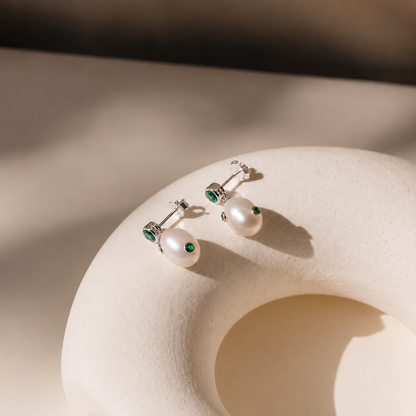 Pair of pearl earrings with green gemstones on a beige stone surface