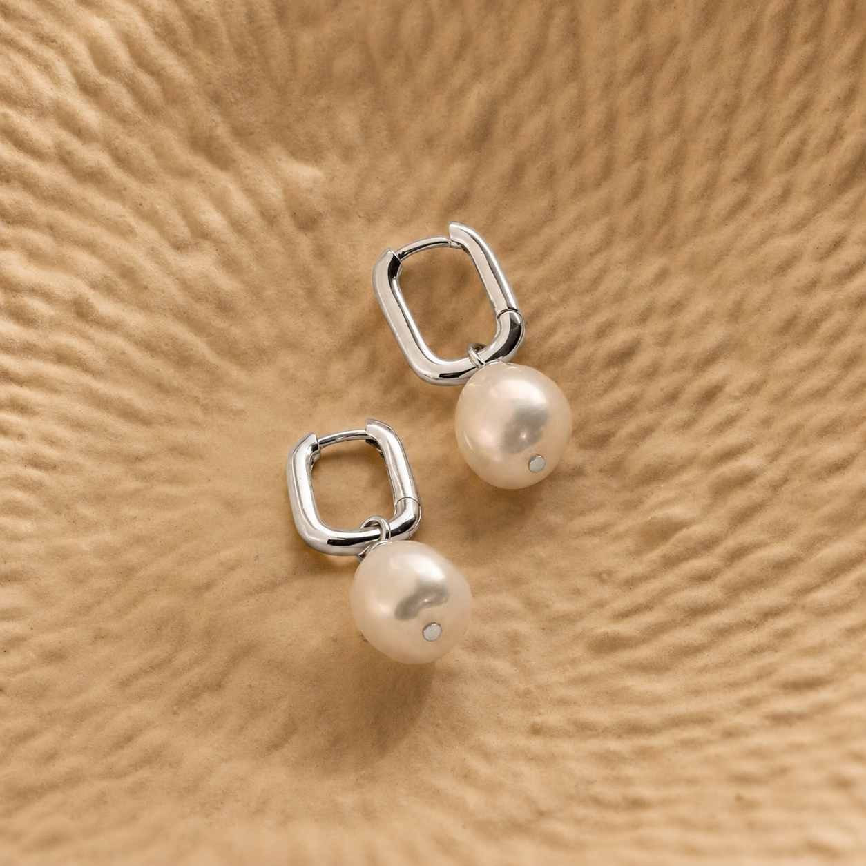 Pair of pearl earrings with silver hoop designs on a beige textured background