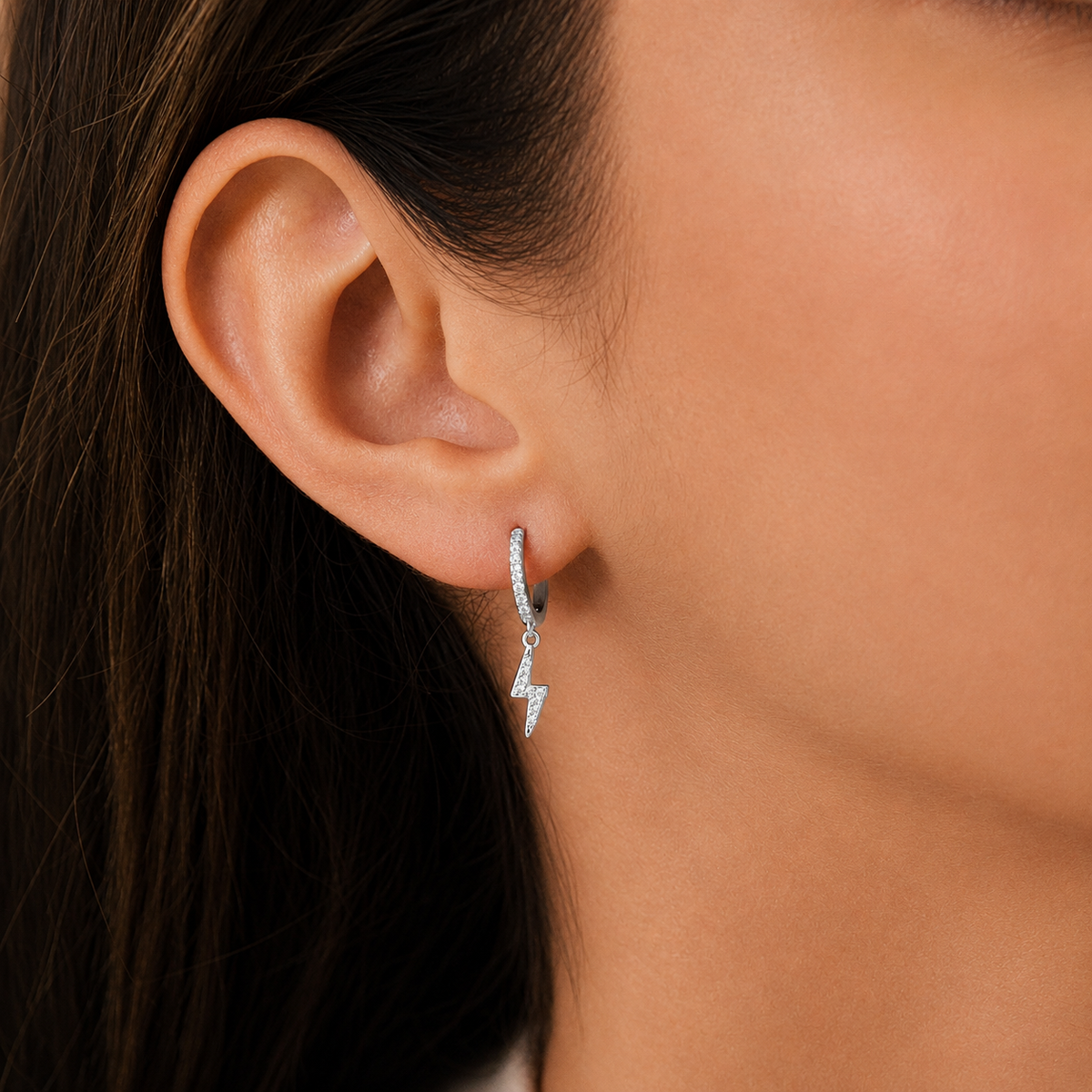 Close-up of an ear wearing a silver hoop earring with a small pendant.