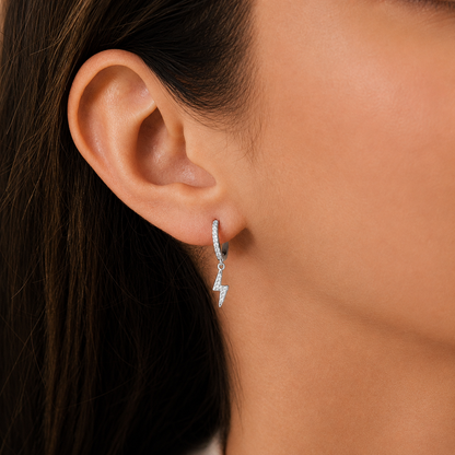 Close-up of an ear wearing a silver hoop earring with a small pendant.