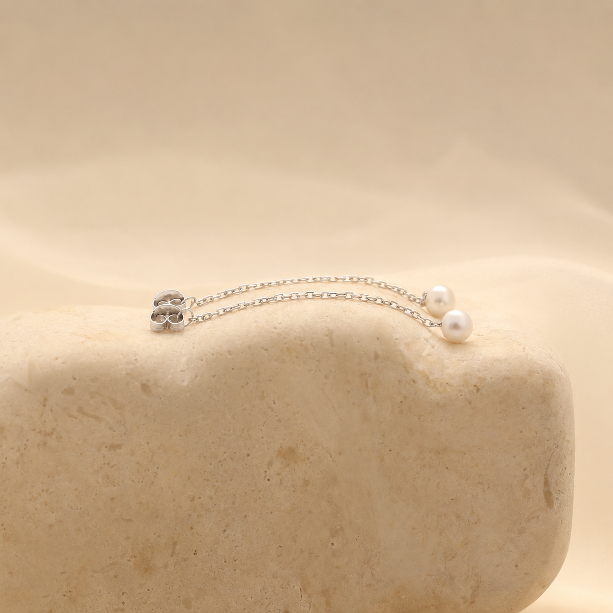 Silver necklace with pearls on a beige stone surface