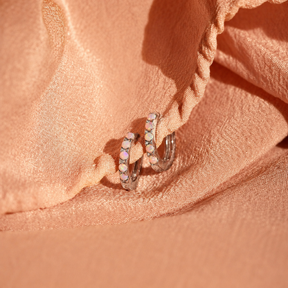 Pair of silver hoop earrings with small stones on a pink fabric background