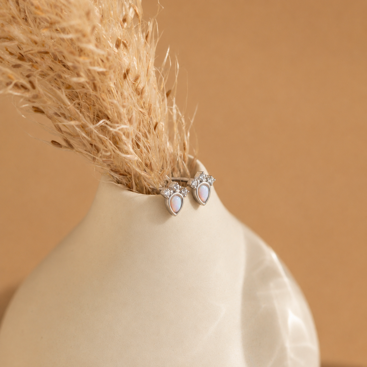 Pair of earrings on a white vase with a beige background