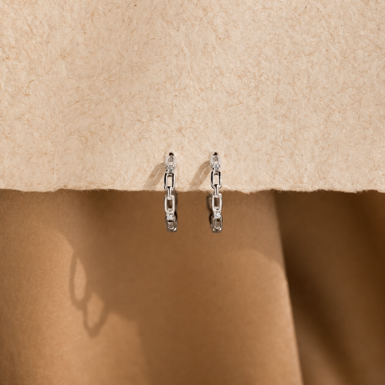 Pair of silver chain earrings on a beige fabric background