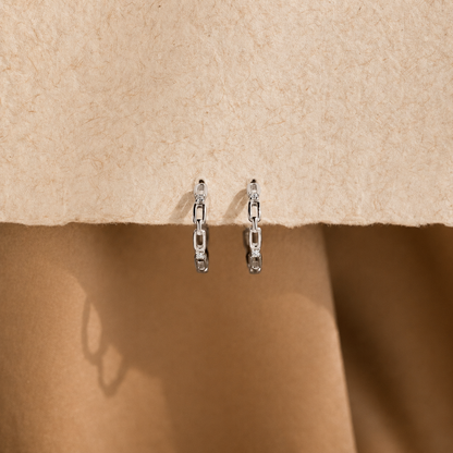 Pair of silver chain earrings on a beige fabric background