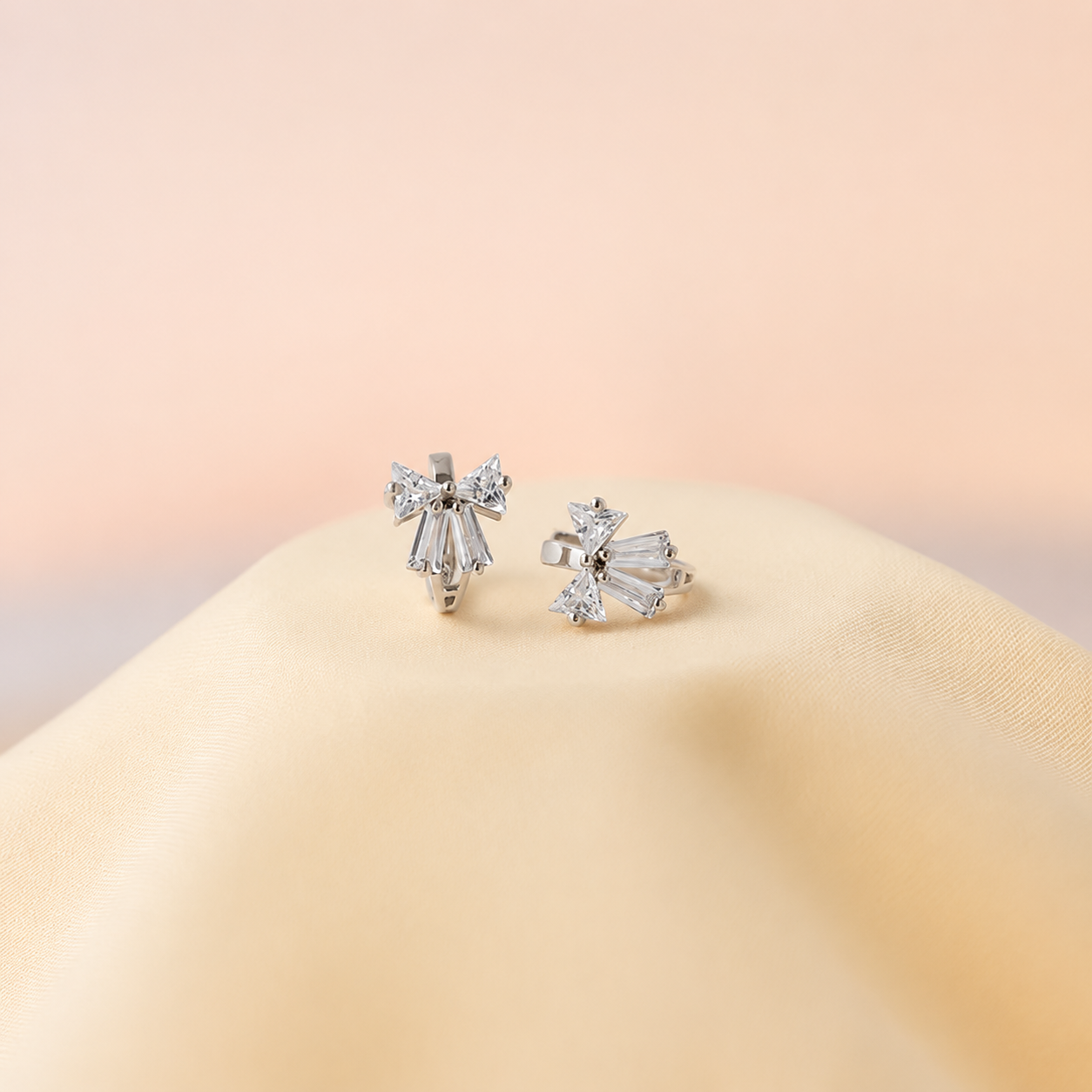 Pair of silver stud earrings on a beige surface with a soft pink background