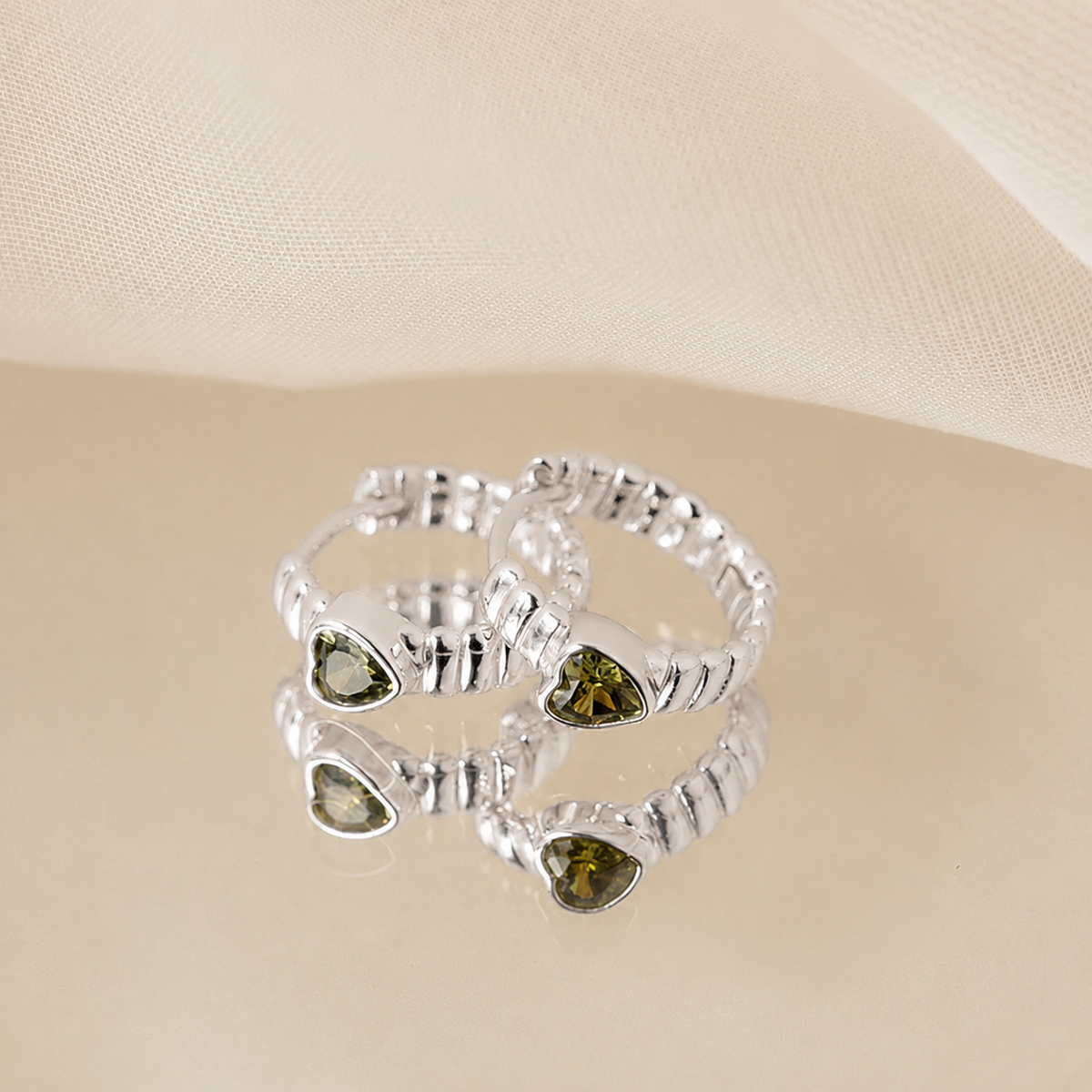 Silver ring with heart-shaped green gemstones on a beige background