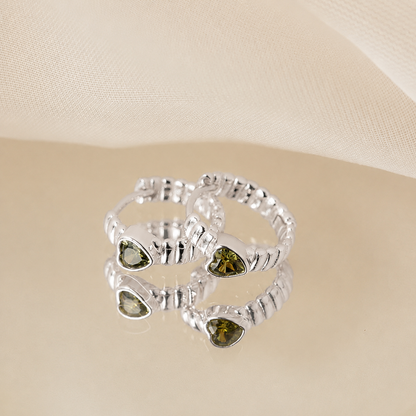 Silver ring with heart-shaped green gemstones on a beige background