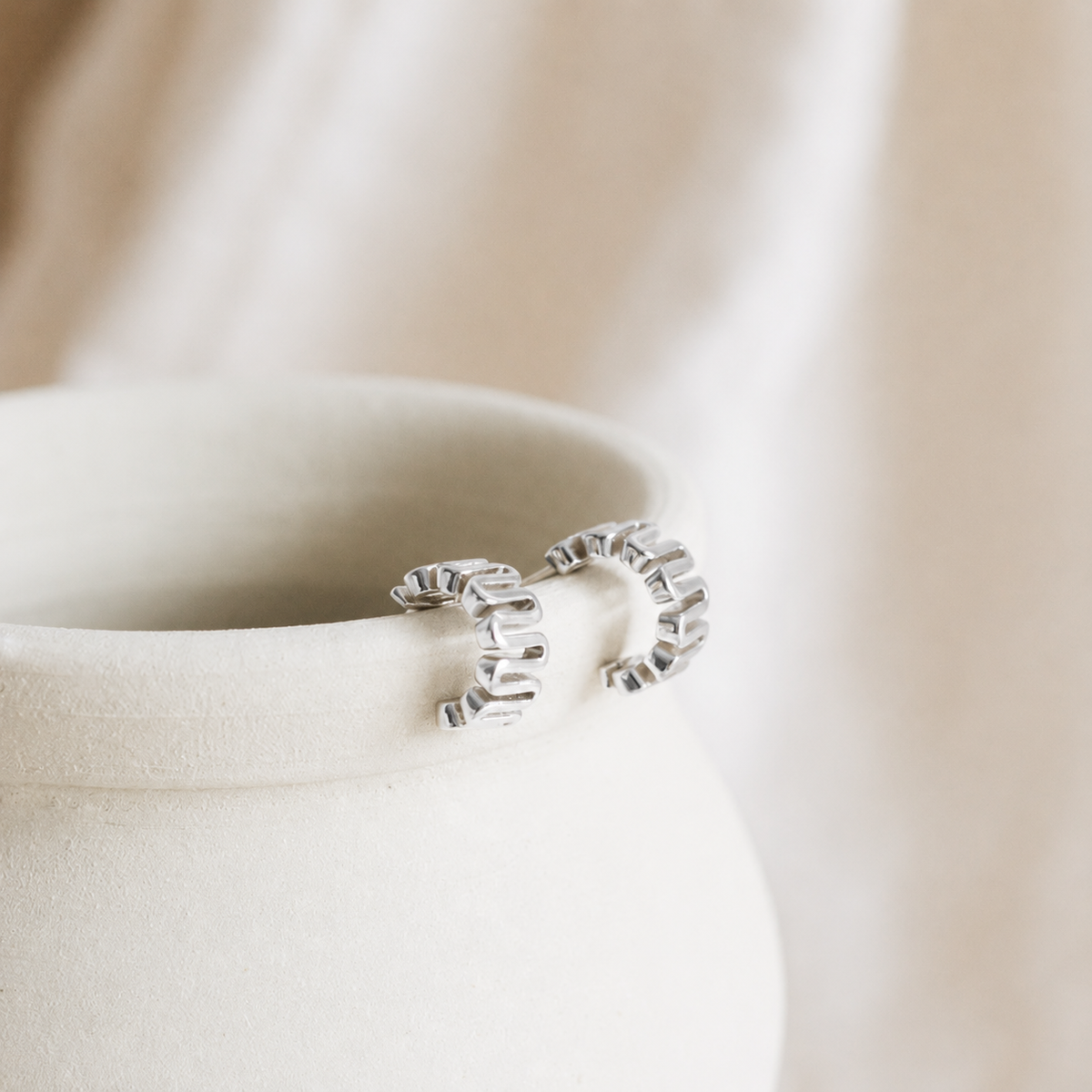 Silver earring on a soft beige fabric background