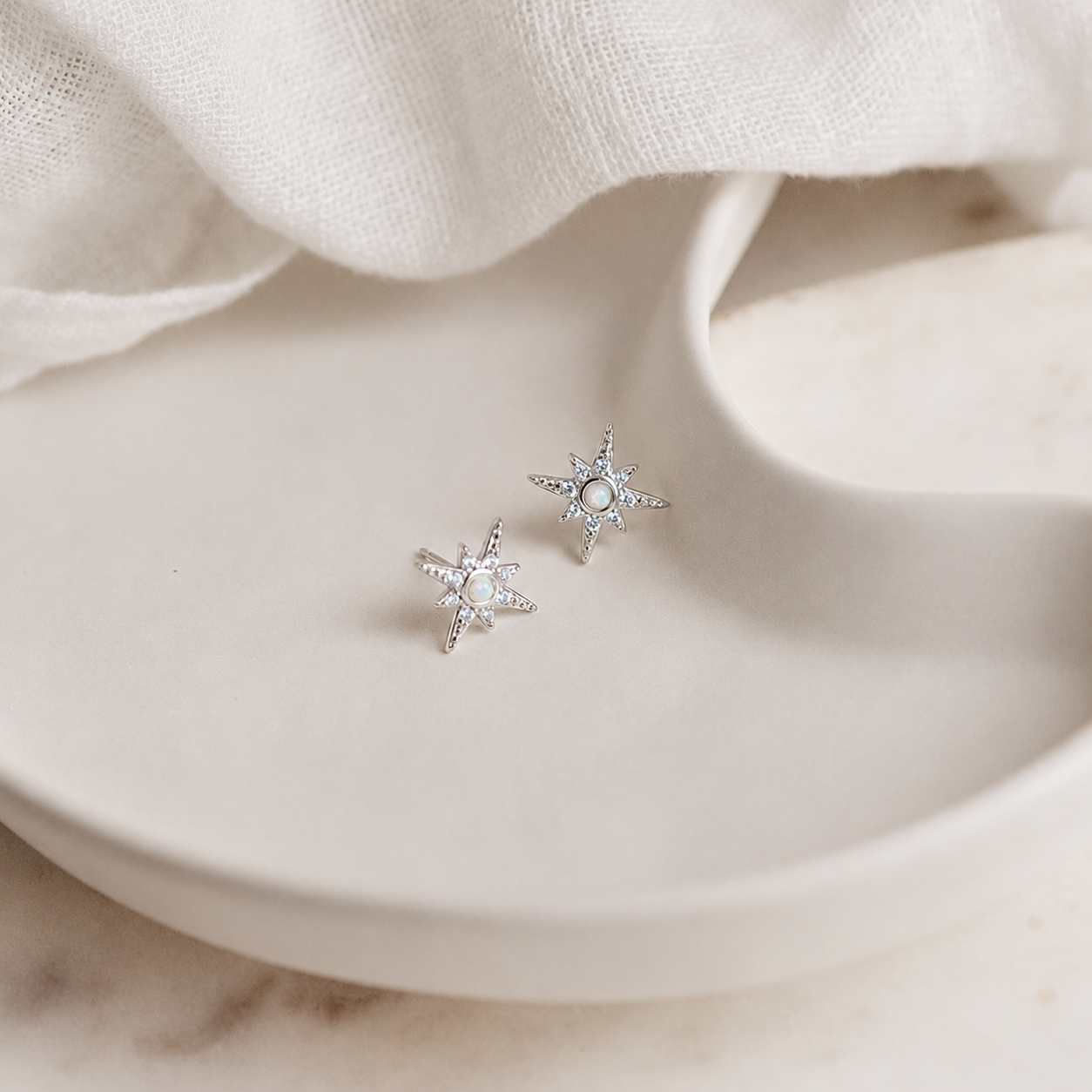 Silver star-shaped earrings on a beige fabric background