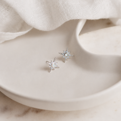 Silver star-shaped earrings on a beige fabric background