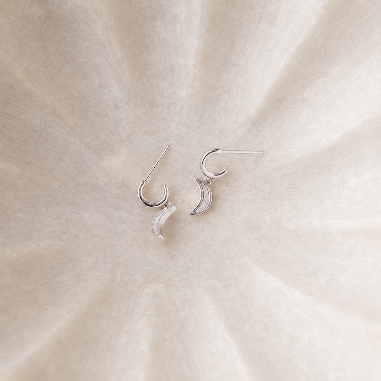 Silver crescent moon earrings on a beige fabric background