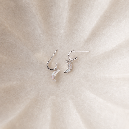 Silver crescent moon earrings on a beige fabric background