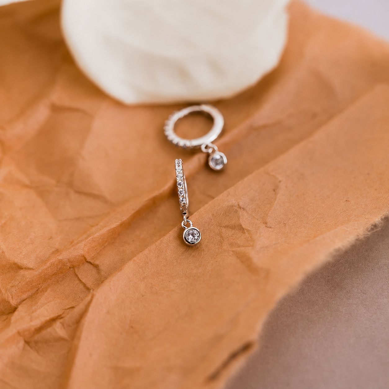 Silver hoop earrings with small round stones on a textured brown surface.