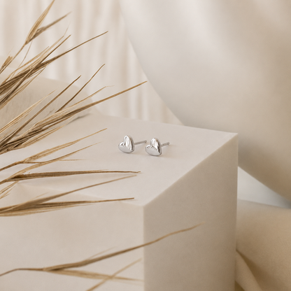 Silver heart-shaped earrings on a beige cube with dried grasses.