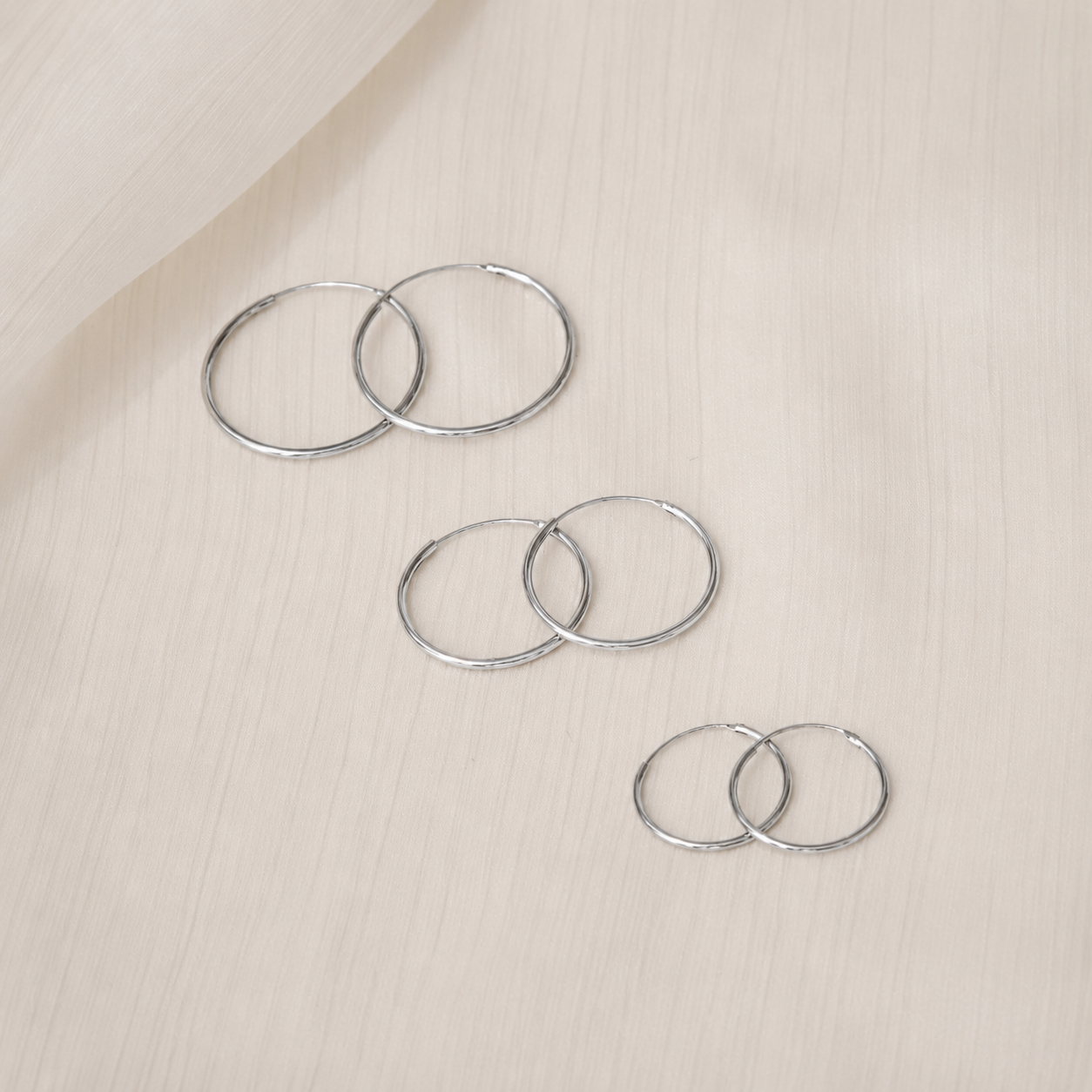 Set of silver hoop earrings on a beige surface