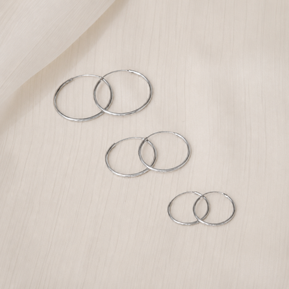 Set of silver hoop earrings on a beige surface