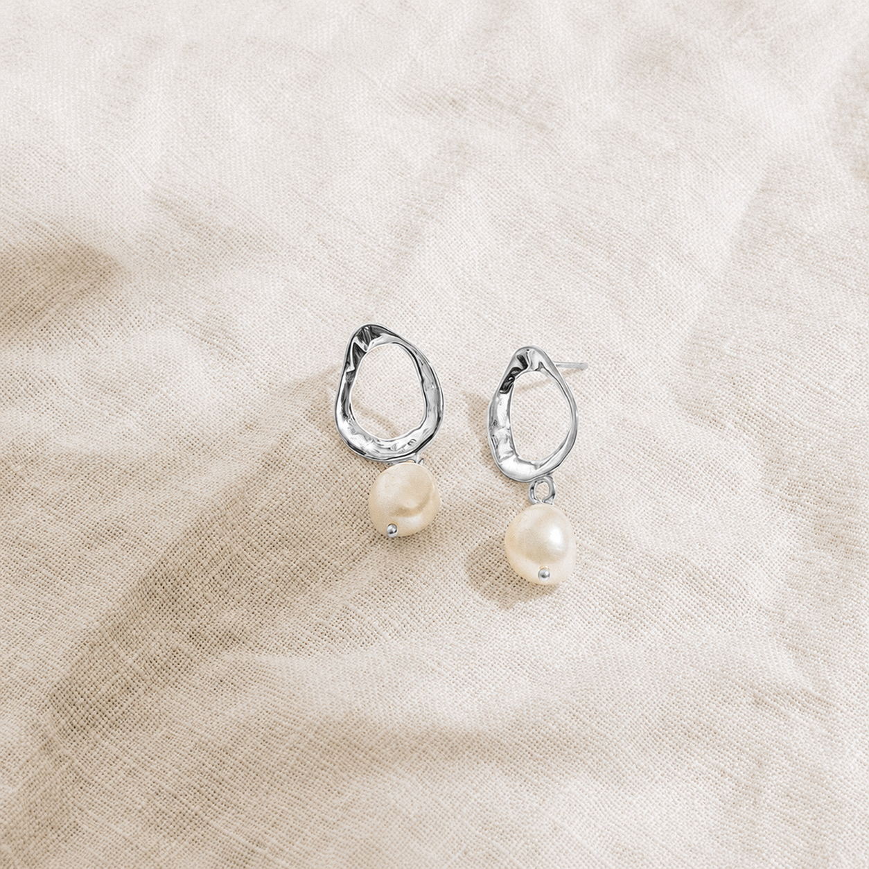 Silver earrings with pearl drops on a beige fabric background
