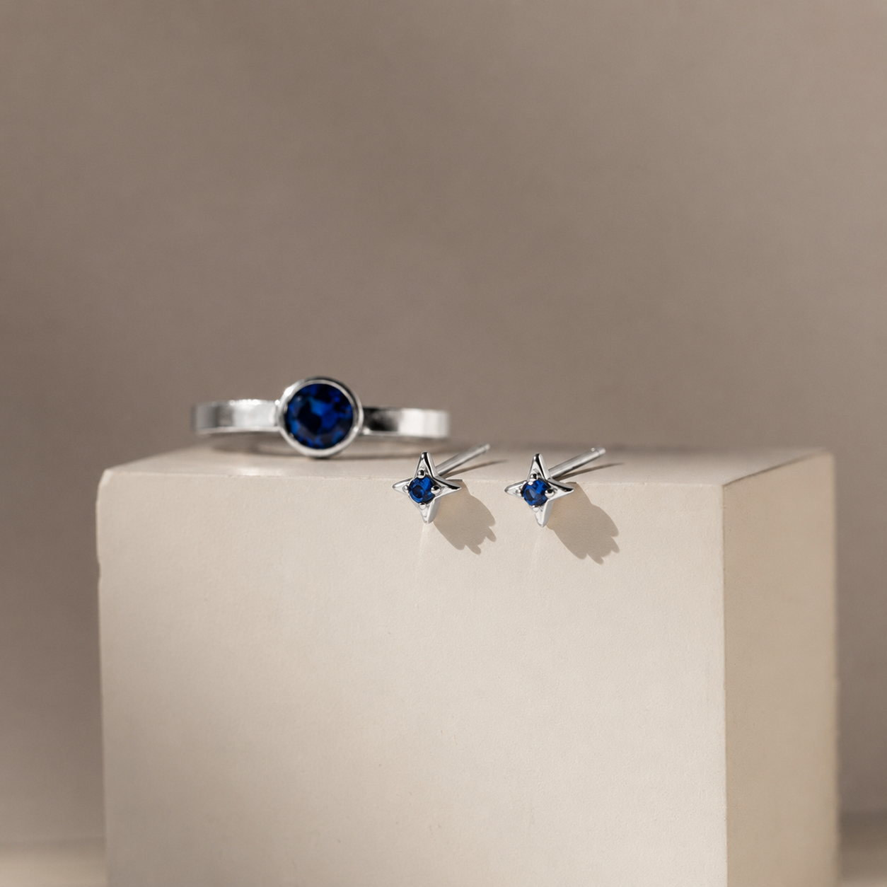 Silver ring and earrings with blue gemstones on a beige cube against a beige background