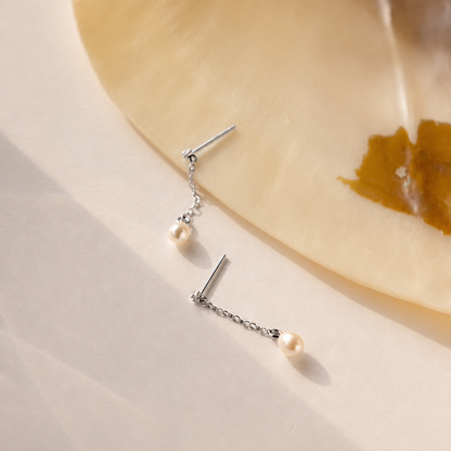 Pearl earrings on a beige surface with a ceramic plate in the background
