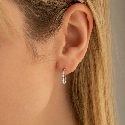 Close-up of an ear wearing a silver hoop earring with blonde hair.