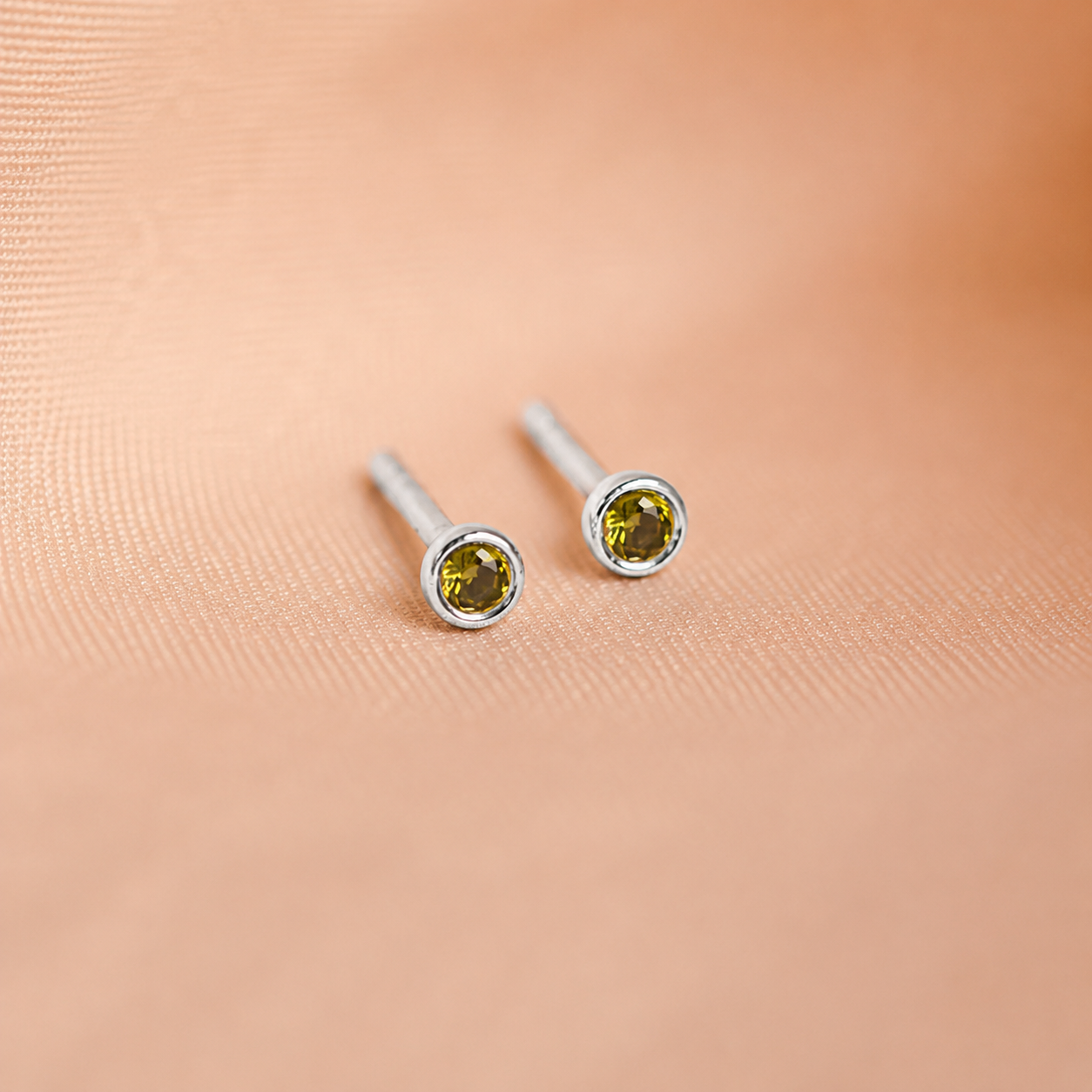 Pair of silver stud earrings with green gemstones on a beige background