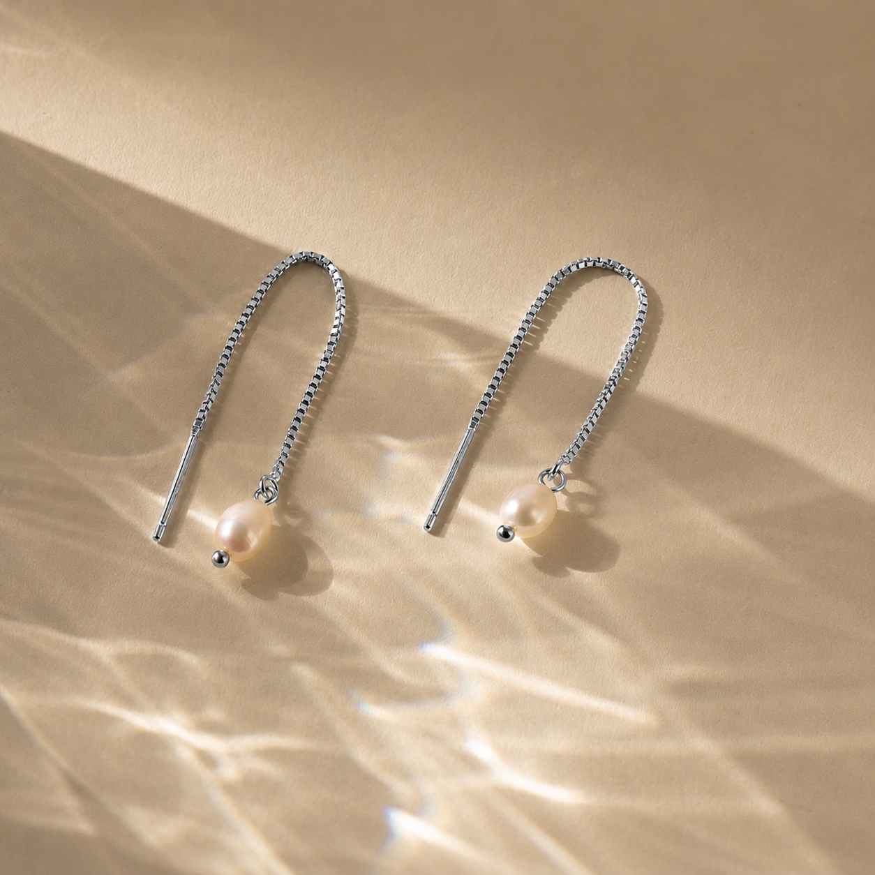 Pair of silver threader earrings with pearls on a beige background