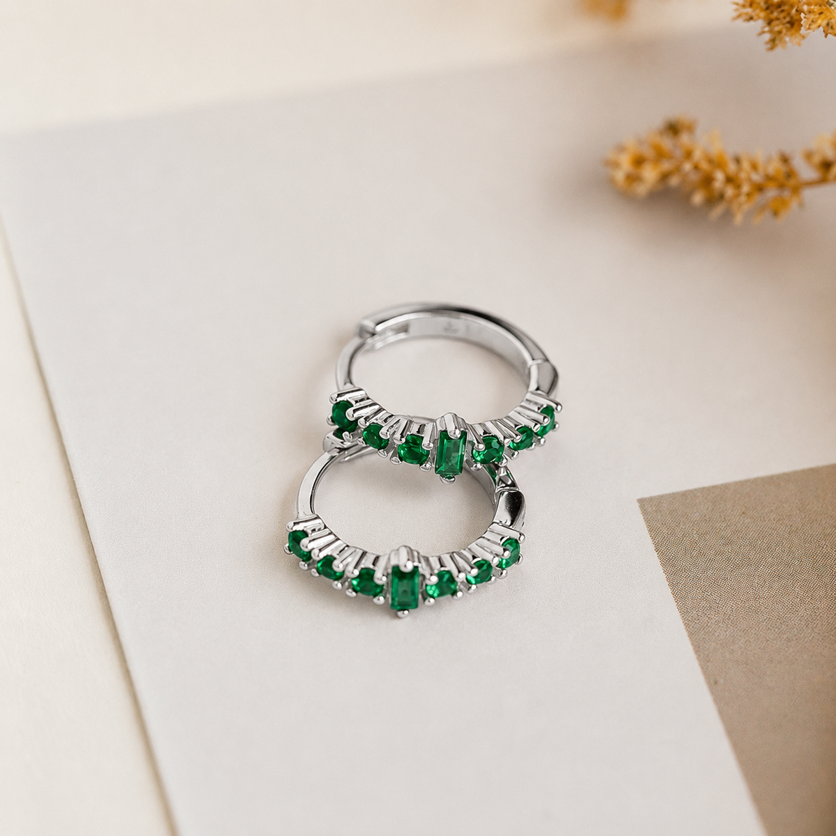 Silver hoop earrings with green gemstones on a light background