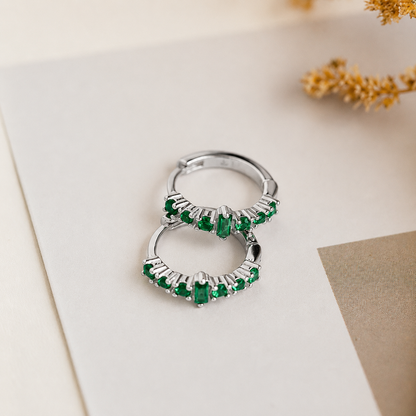 Silver hoop earrings with green gemstones on a light background