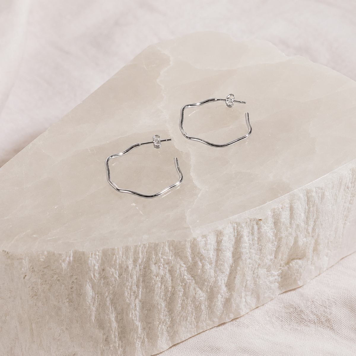 Hexagonal hoop earrings on a textured beige surface