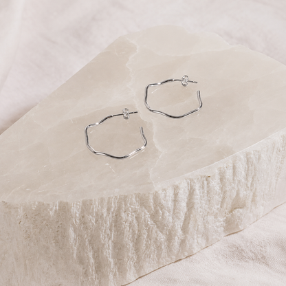 Hexagonal hoop earrings on a textured beige surface