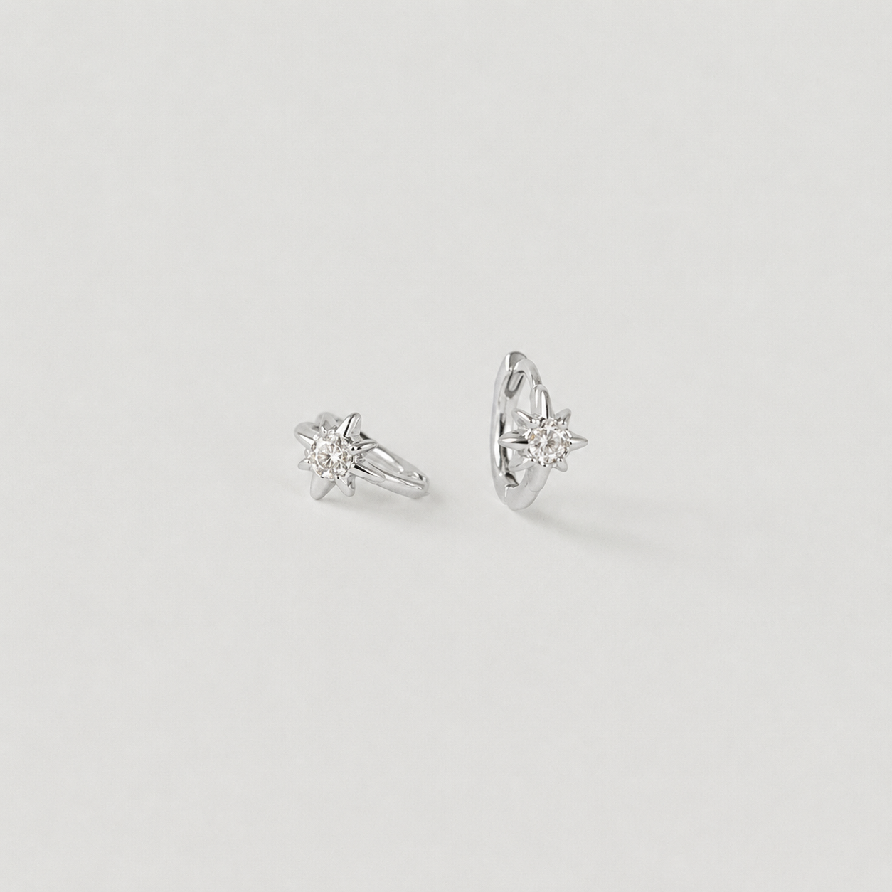 Pair of silver earrings with clear gemstones on a light gray background