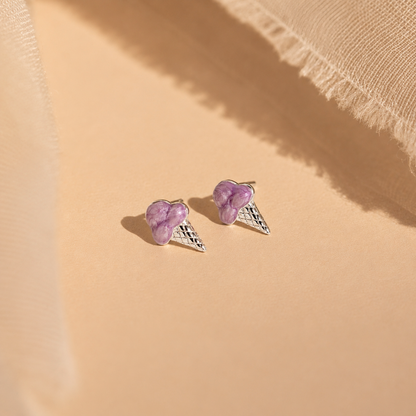 Pair of purple heart-shaped earrings with silver wings on a beige fabric background