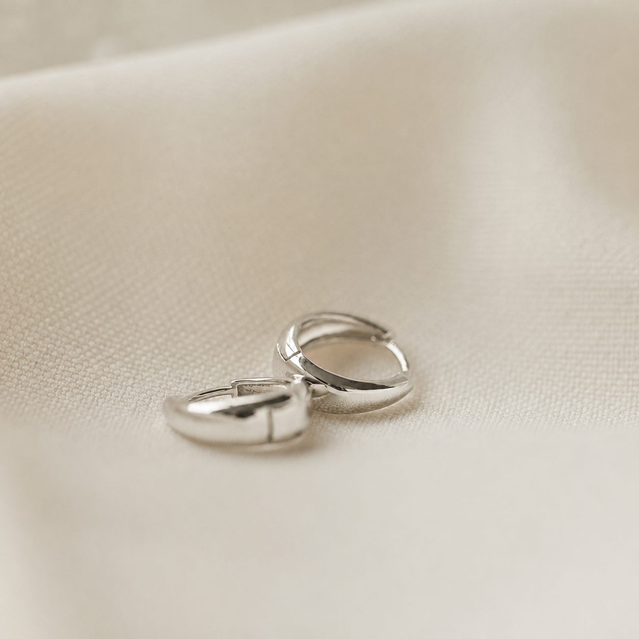 Two silver hoop earrings on a beige fabric background