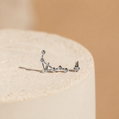 Silver constellation earrings on a beige stone with a beige background
